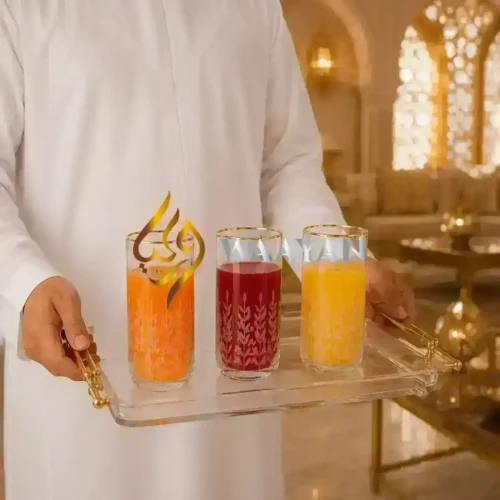 Elegant glass tumblers with gold accents, featuring a floral design, holding orange, red, and yellow juices on a tray.