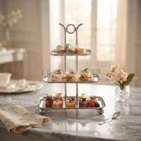 Three-tier serving stand in polished silver stainless steel with looped top handle and rectangular trays on ball feet.