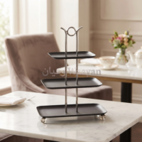 Three-tier serving stand with matte black metal trays, brushed stainless steel posts and ring handle, and silver ball feet