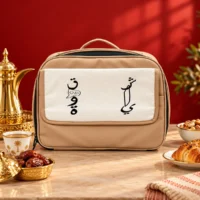D7AACA1C-4FBF-4F5F-B42D-443BCF670171 Beige fabric insulated carrying bag with white canvas flap and black Arabic script, top handle and zip closure, front view