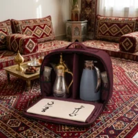 Gemini_Generated_Image_14toja14toja14to Interior view of maroon fabric travel bag with silver metal dallah pot with brushed gold lid and matte blue thermal carafe