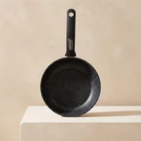 Black speckled nonstick frying pan with a matte black long handle, hanging hole, and small metal badge on the handle