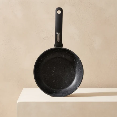 Black speckled nonstick frying pan with a matte black long handle, hanging hole, and small metal badge on the handle