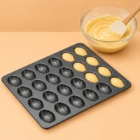 Mini Madeleine Pan, 24 Cavities, Non-Stick Mini madeleine pan shown with batter in several shell-shaped cavities